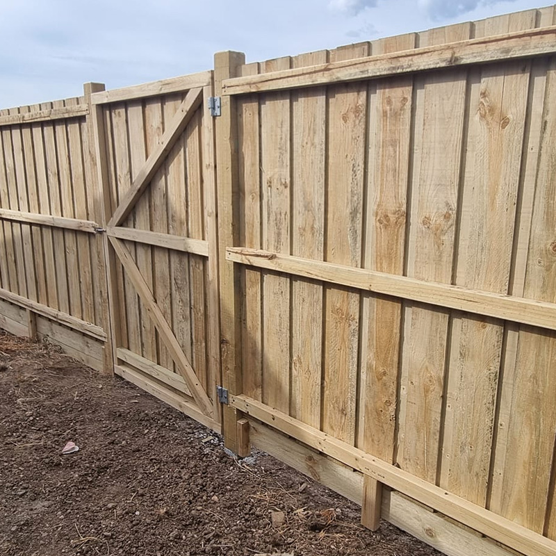 New timber paling fence with a braced gate on bare soil